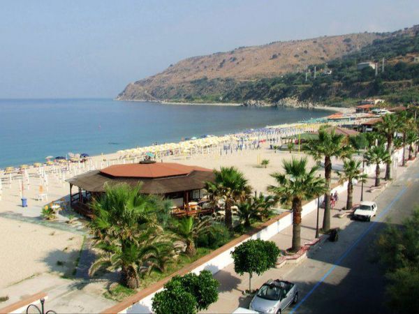 Spiaggia con palme, mare calmo e colline sullo sfondo.
