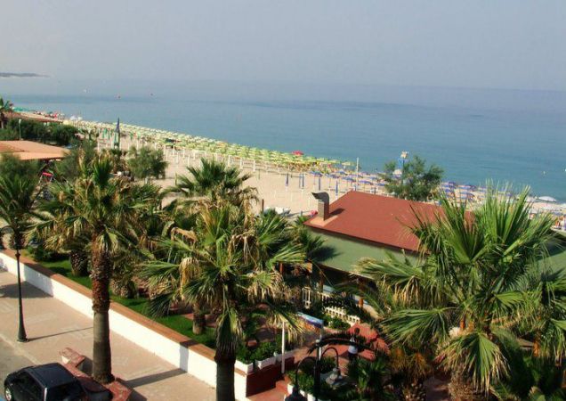 Una spiaggia con lettini e ombrelloni, circondata da palme, vista dall'alto.