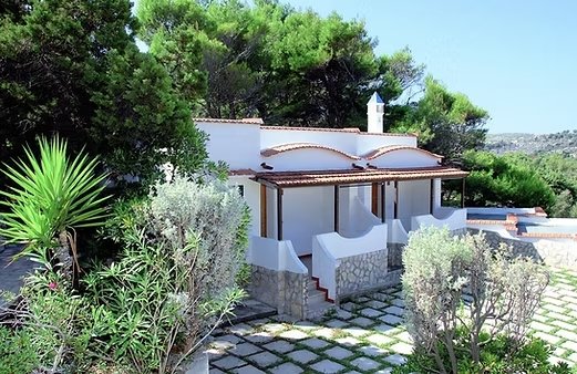Casa bianca con tetto curvo e giardino ricco di vegetazione.