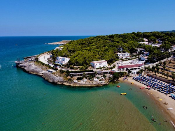 Vista aerea di una baia con spiaggia, case e ombrelloni.