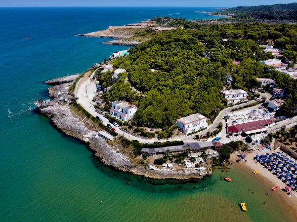 Baia con vegetazione, strutture costiere, e spiaggia con ombrelloni.