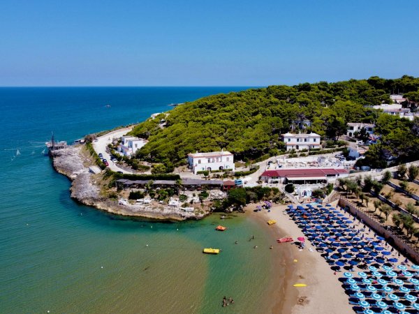 Una spiaggia sabbiosa con ombrelloni blu e un promontorio alberato vicino al mare.