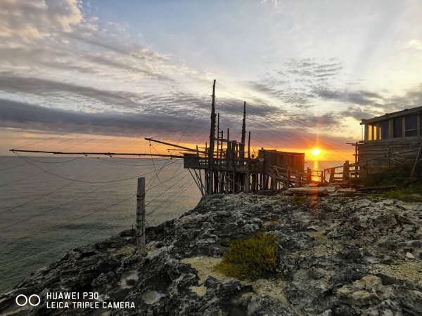 Un trabucco di legno al tramonto, con il sole che si riflette sull'acqua.