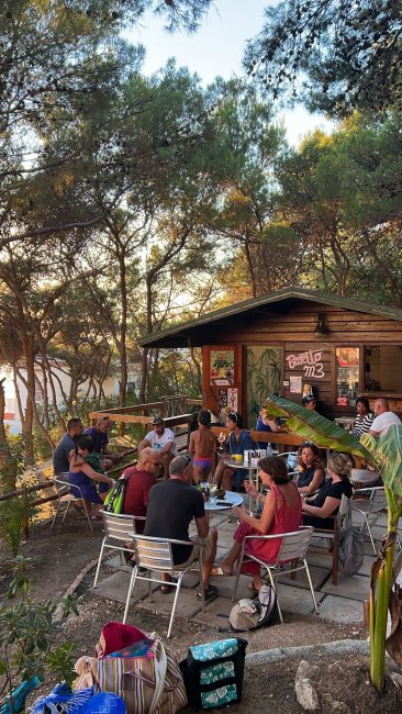 Gruppo di persone sedute all'aperto in un bar tra gli alberi.