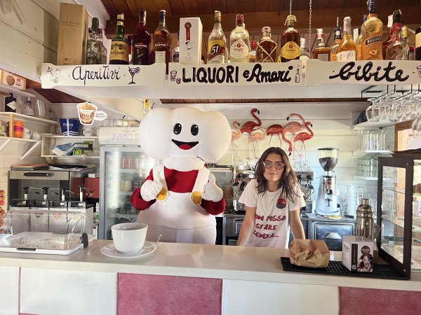 Barista e mascotte in un bar con bottiglie di alcolici.