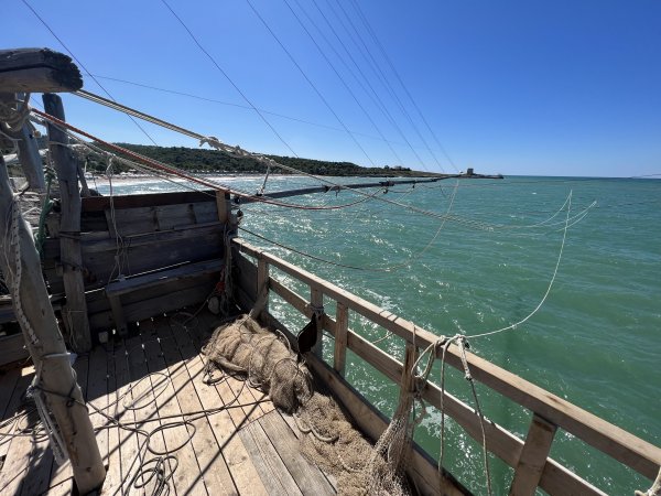 Una piattaforma di legno sul mare con reti da pesca, sotto un cielo blu limpido.