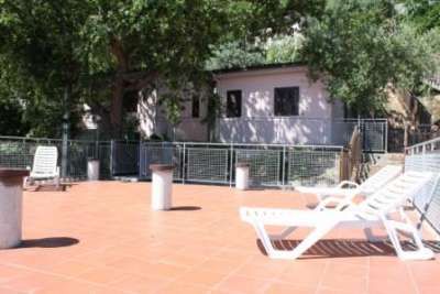 Terrazza con lettini prendisole, alberi e edificio sullo sfondo.