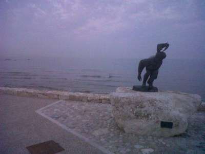 Statua su pietra vicino al mare, oceano calmo al tramonto.
