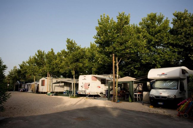 Camping con roulotte e tende sotto gli alberi.