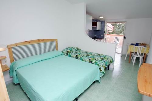 Una camera con letto matrimoniale, letto singolo e tavolo da pranzo, vista su balcone.