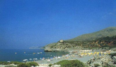Spiaggia affollata con ombrelloni colorati, colline sullo sfondo.