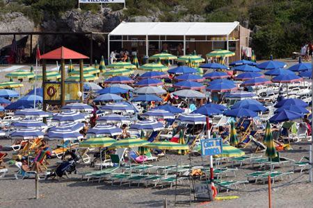 Spiaggia affollata con molti ombrelloni blu e gialli, area di relax.