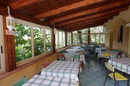 Una veranda con tavoli a quadretti, sedie colorate e finestre ampie.