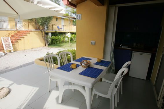 Tavolo bianco con quattro sedie e tovagliette blu su una veranda.