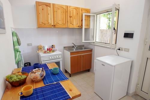 Cucina semplice con tavolo apparecchiato e mobili in legno chiaro.