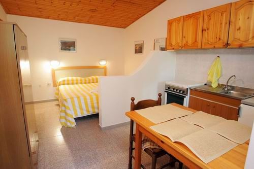 Camera con letto a righe gialle e angolo cottura in legno chiaro.