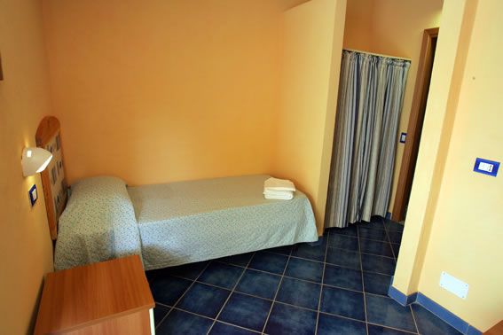 Camera con letto singolo coperto da trapunta azzurra, pavimento blu e tende a righe.