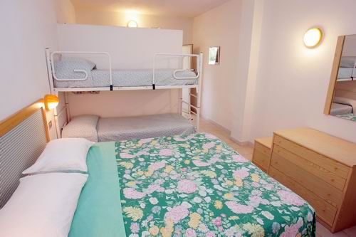 Camera con letto matrimoniale floreale, letto a castello bianco e arredi semplici.