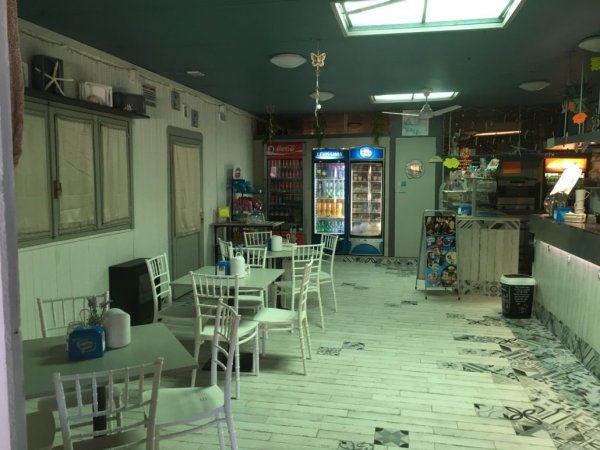 Interno di una caffetteria con sedie bianche e frigoriferi.