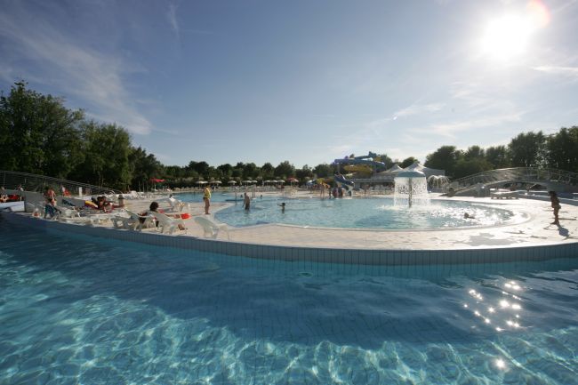 Piscina all'aperto con fontana e persone che nuotano.