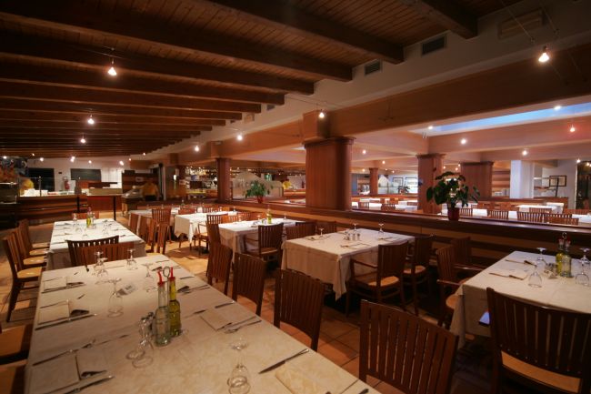 Un ristorante con tavoli apparecchiati, sedie in legno e soffitto a travi di legno.
