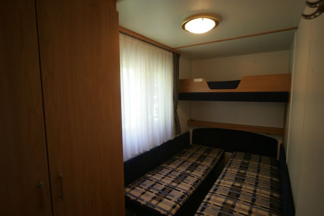 Cameretta con letto a castello e due letti singoli, tenda bianca.