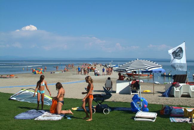Persone su una spiaggia, alcune sotto un ombrellone. Il mare si estende all'orizzonte.
