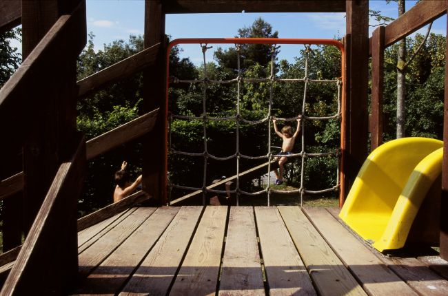 Parco giochi con scivolo giallo e rete da arrampicata. Due bambini giocano.
