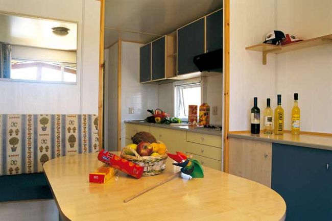 Interno di una casa mobile con cucina e tavolo, decorato con frutta e bottiglie.