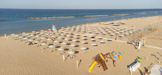 Spiaggia con ombrelloni bianchi e area giochi.