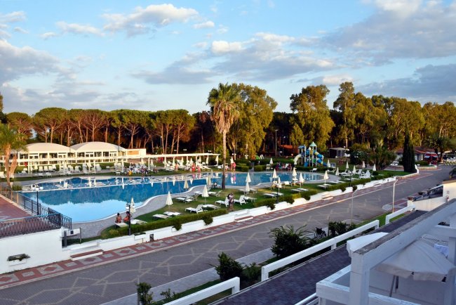 Piscina circondata da ombrelloni e vegetazione.