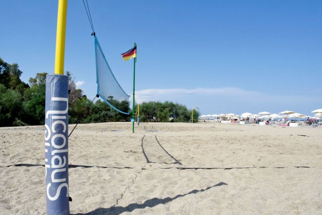 Spiaggia con rete da beach volley e ombrelloni.