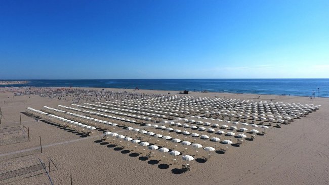 Ampia spiaggia con file di ombrelloni bianchi.