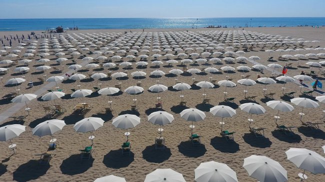 Spiaggia con molti ombrelloni bianchi su sabbia.