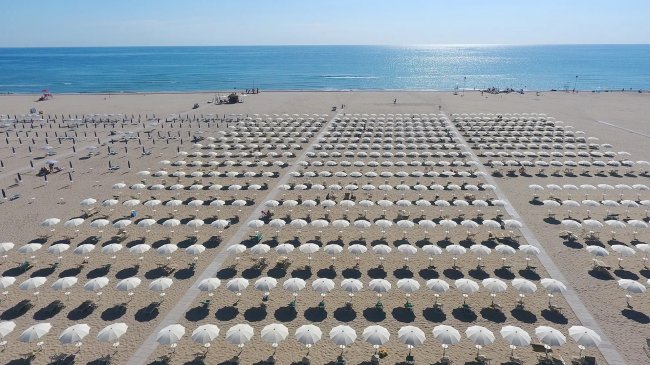 Spiaggia con file di ombrelloni bianchi.
