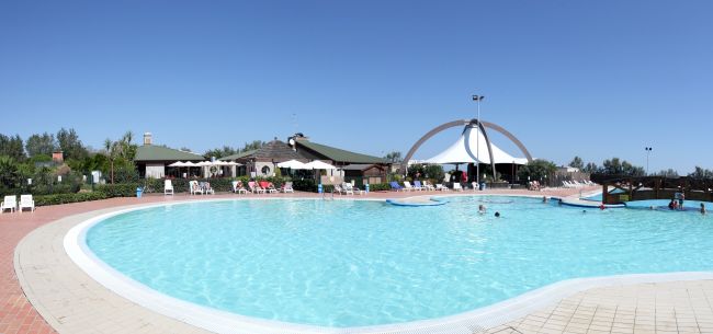 Piscina ampia con pochi bagnanti e strutture in lontananza.