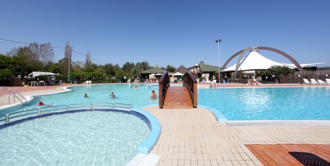 Passerella in legno tra due piscine illuminate dal sole.