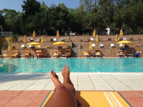 Persona su sdraio bordo piscina con ombrelloni gialli.