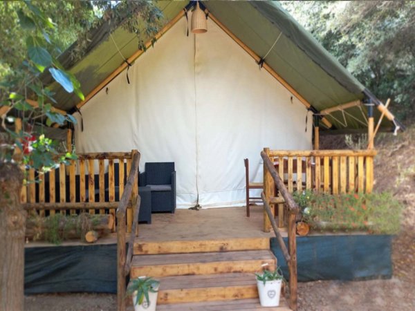 Tenda glamping con veranda in legno e sedie.