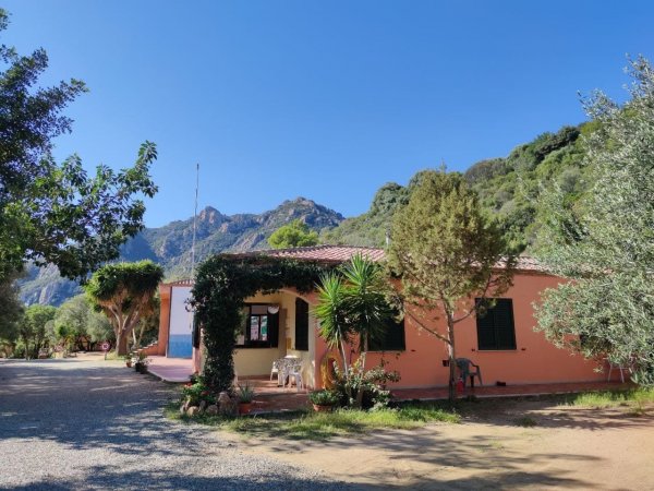 Casa rosa tra gli alberi con montagne sullo sfondo.