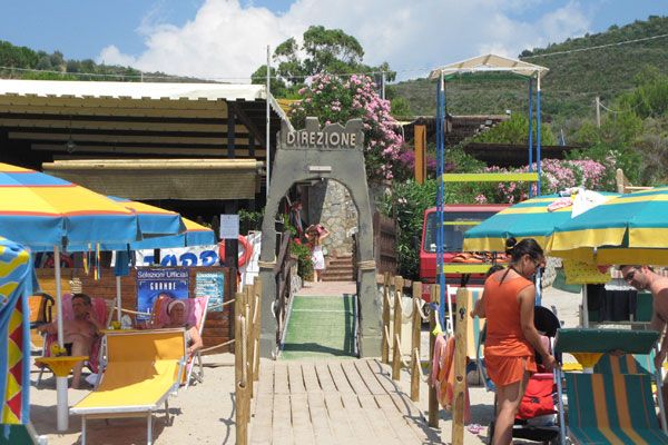 Area spiaggia con sedie a sdraio gialle, parasole colorati e cartello 