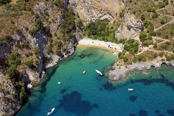 Una piccola baia con acque blu, imbarcazioni e una spiaggia nascosta circondata da scogli.