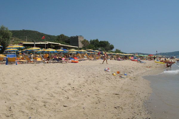 Spiaggia con ombrelloni gialli e blu e torre in lontananza.