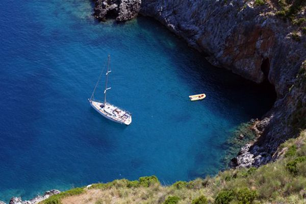 Barca a vela e kayak in mare blu, vicino a una costa rocciosa.