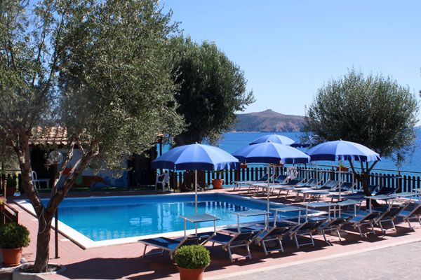 Piscina con lettini blu e ombrelloni, vista mare.
