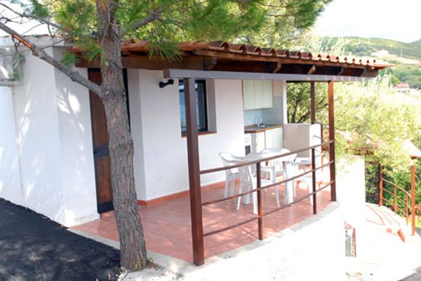 Una casa con portico in legno, due sedie bianche e un tavolo all'aperto.