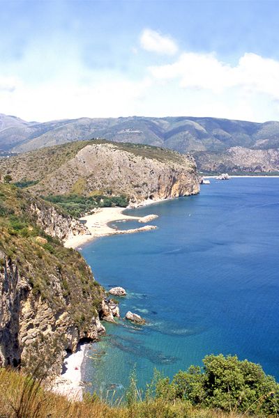 Una costa rocciosa con acqua blu e spiagge sabbiose sotto un cielo limpido.