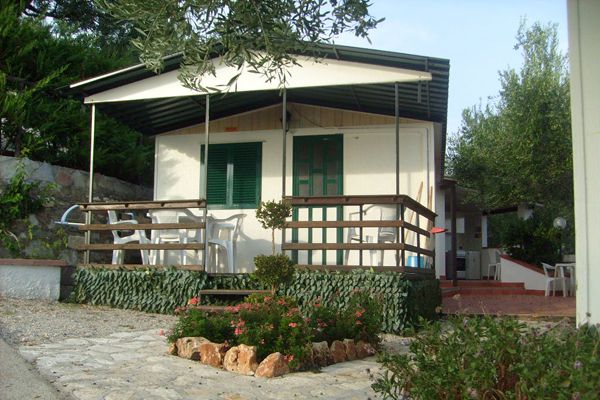 Una casetta con veranda, sedie di plastica e fiori nel cortile.