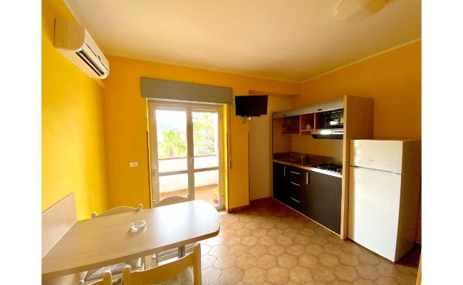 Cucina con pareti gialle, tavolo, sedie, frigorifero e fornello.
