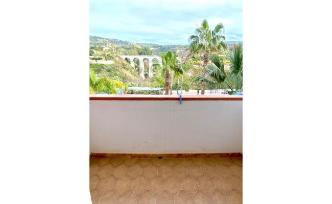Una terrazza con pavimento piastrellato, vista su un viadotto e palme sullo sfondo.